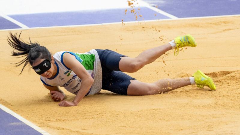 A blindfolded woman landing in a long jump sand pit 