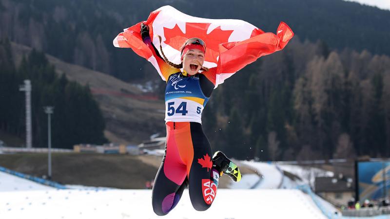 A female Paralympic skier is jumping while holding the Canadian flag