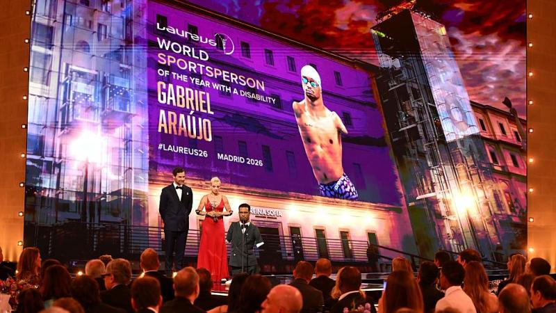 A man with a disability standing on the Laureus Awards stage next to a man and a woman