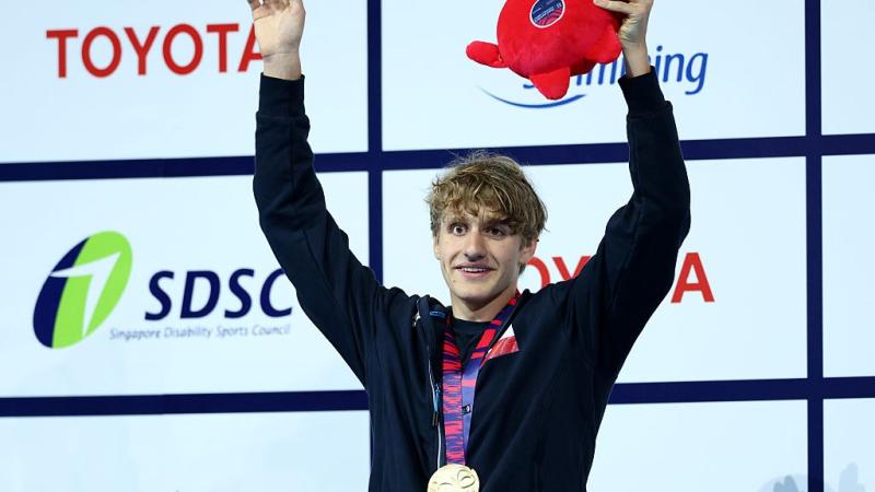 A young male athlete with open arms celebrating with a gold medal 
