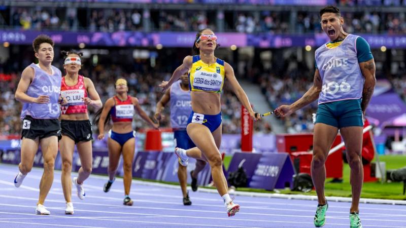 A group female vision impaired sprinters with male guides finishing a race