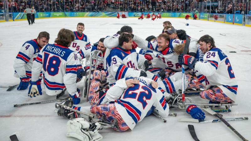 A group of Para ice hockey athletes from USA celebrate in the middle of a rink