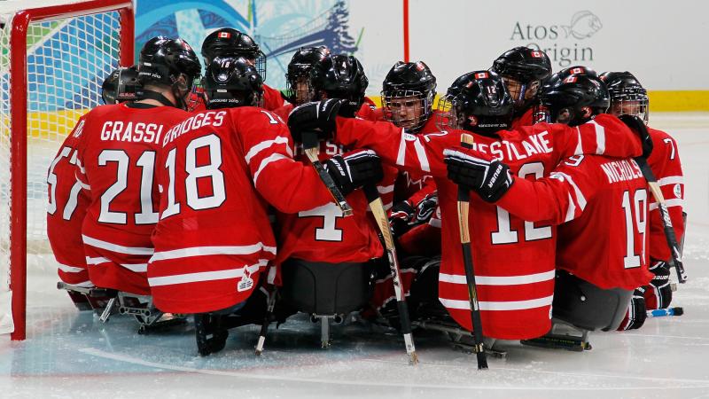 The Canadian Ice Sledge Hockey Team gathered around the goal.