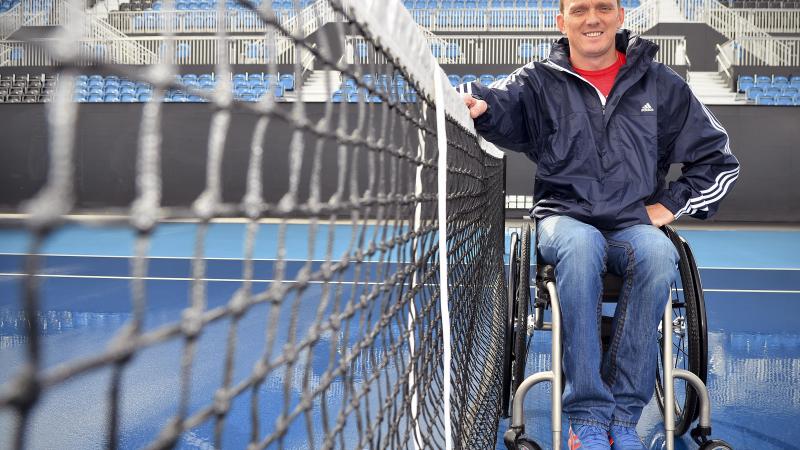 A picture of an athlete in a wheelchair next to a tennis let.