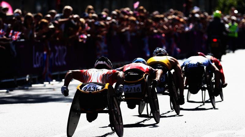 group of men in racing wheelchairs pass spectators