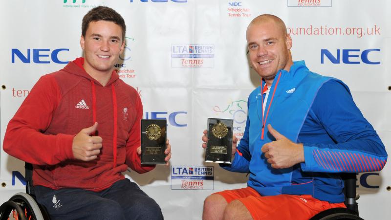 A picture of 2 men in a wheelchair showing their trophies