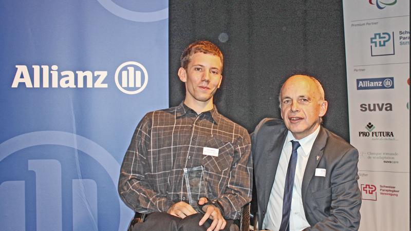 A picture of a man in a wheelchair posing with his award