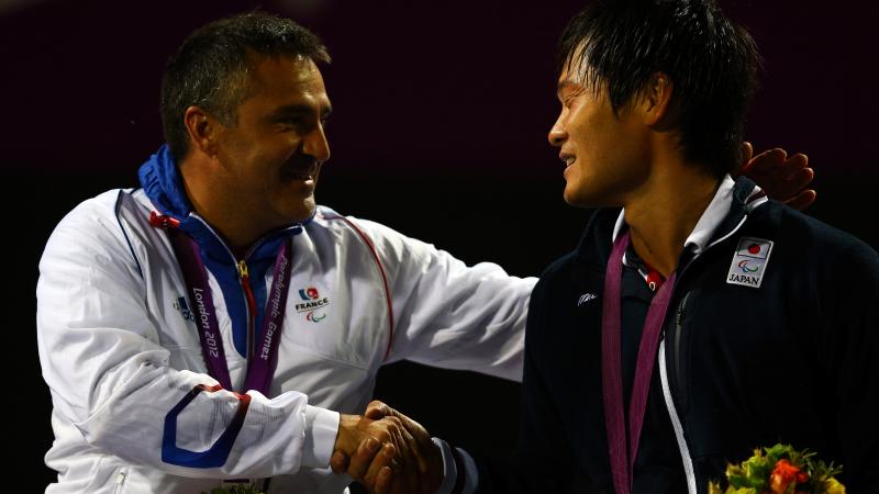 A picture of two men in a wheelchair shaking their hands