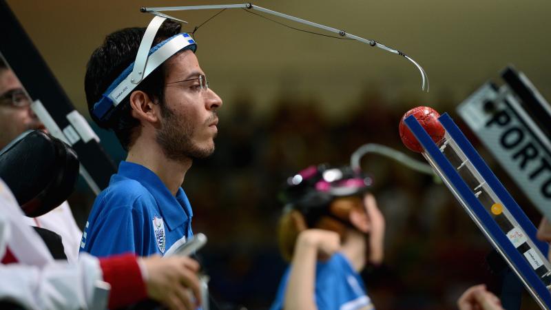 A picture of a man pushing a smal ball with a metal arm hooked to his head