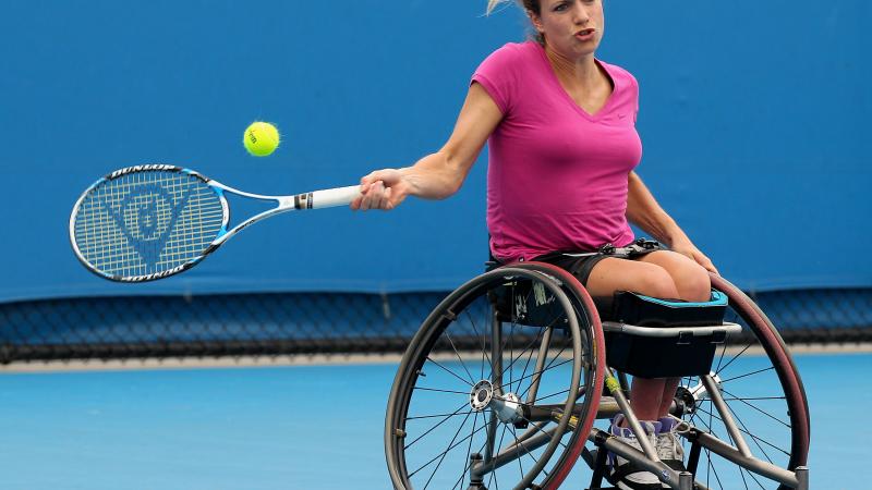 Female wheelchair tennis player in action on a blue court
