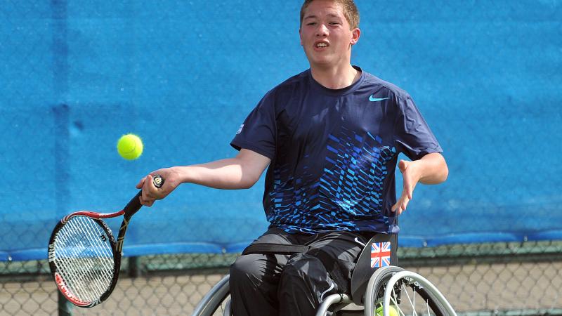 A picture of a young man in a wheelchair playing a forhand in a wheelchair tennis match