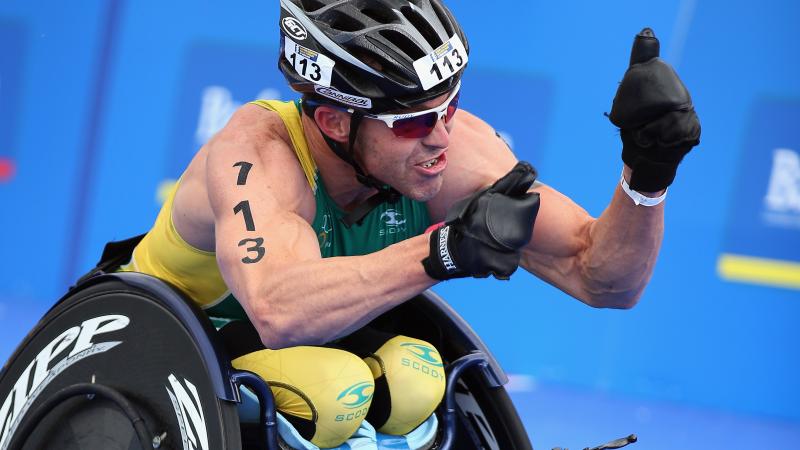 A picture of a man in a wheelchair celebrating his victory after a para-triathlon