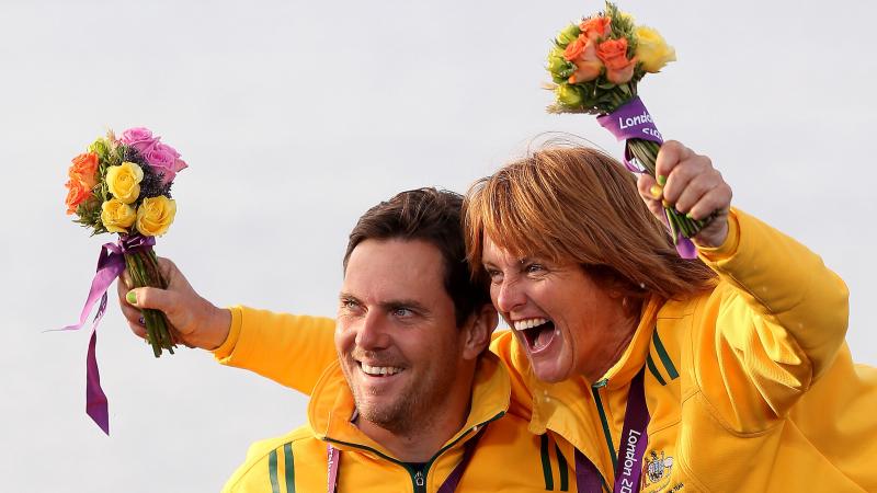 A picture of a man in a wheelchair and woman celebrating their victory with a gold medal around their necks