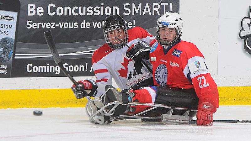 A picture of a two men in sledges playing ice hockey