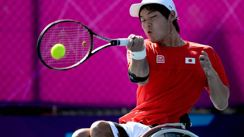 A picture of man in a wheelchair playing a forehand in a tennis match