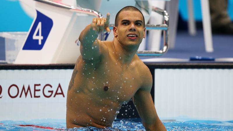 A picture of a man in the pool sitting on the swimming line with his hand up 