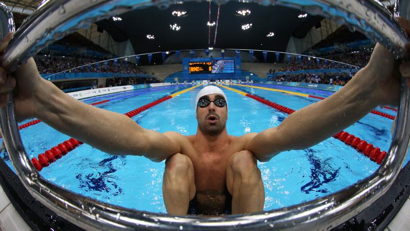 A picure of a man in the pool holding starting block with his hands