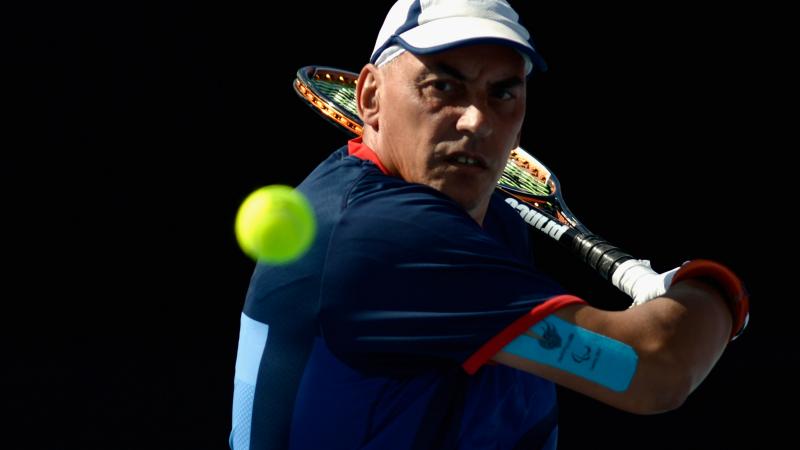 A picture of a man in a wheelchair playing a backhand during a wheelchair tennis match