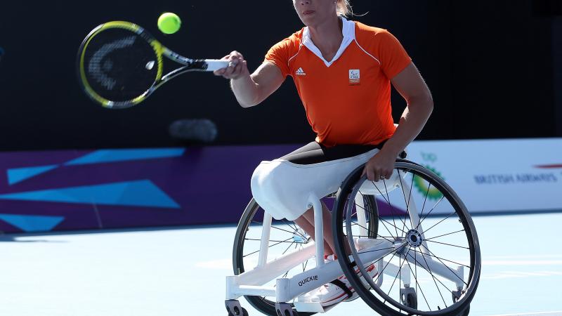 A picture of a woman in a wheelchair playing a forhand during a wheelchair tennis match.