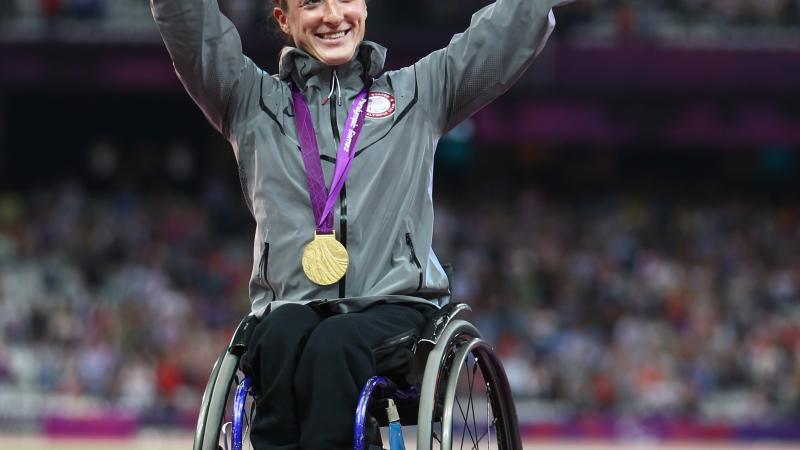 A picture of a woman on a podium with the medal around her neck and with her hands up