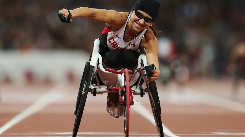 A picture of a woman in the wheelchair on a track celebrating the victory with her hand up