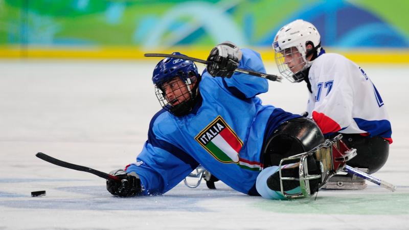A picture of two men in sledges fighting the puck during a ice sledge hockey match