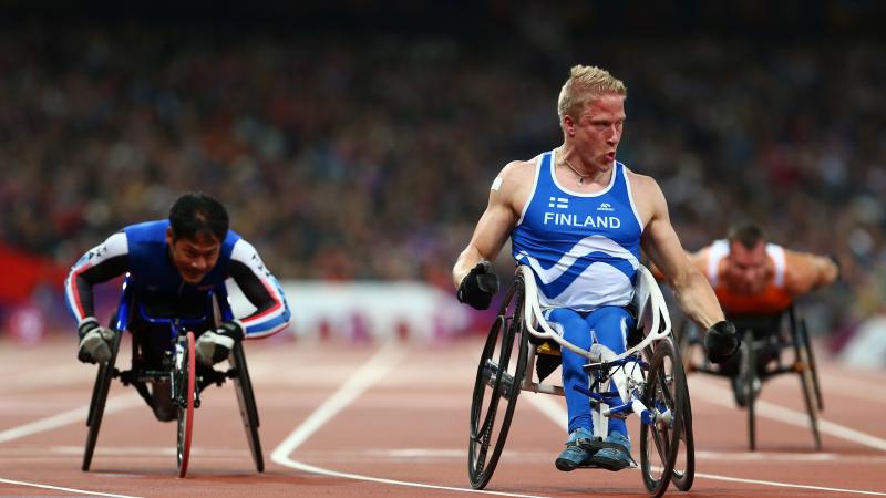 A picture of a man in a wheelchair celebrates on a track after crossing a finish line