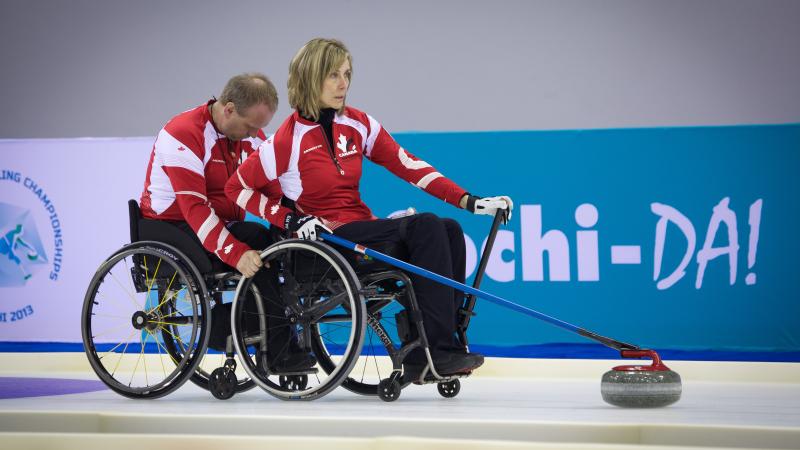 A picture of 2 person in wheelchairs playing curling