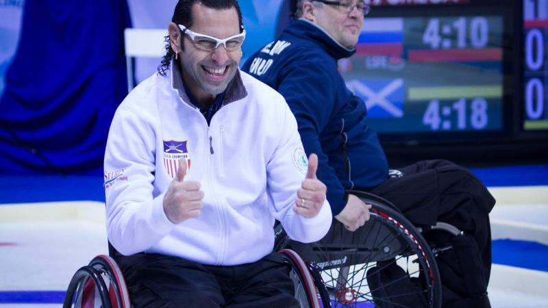 A picture of a man in a wheelchair tumbs up celebrating his victory