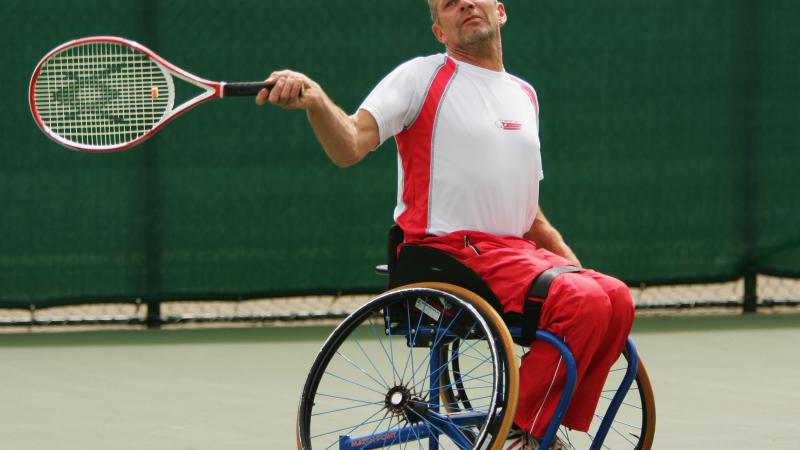 A picture of a man in a wheelchair playing a forehand in a tennis match