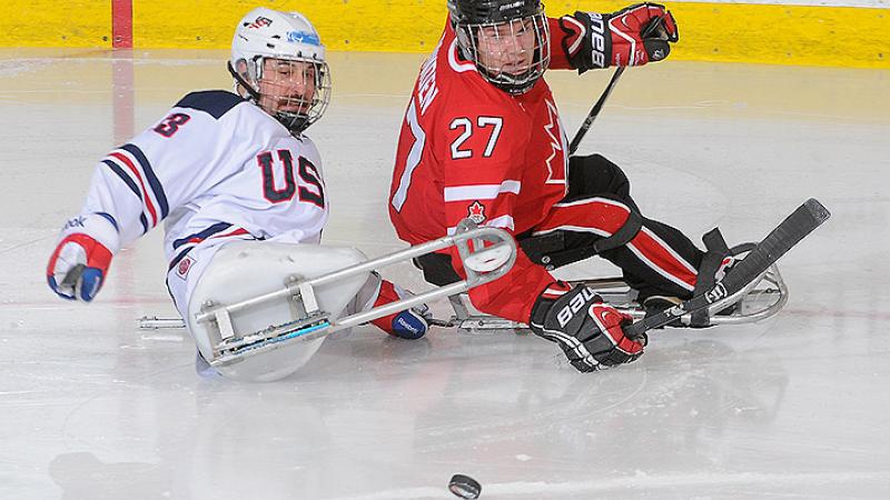 A picture of two mens in sledges fighting for the puck during a hockey match