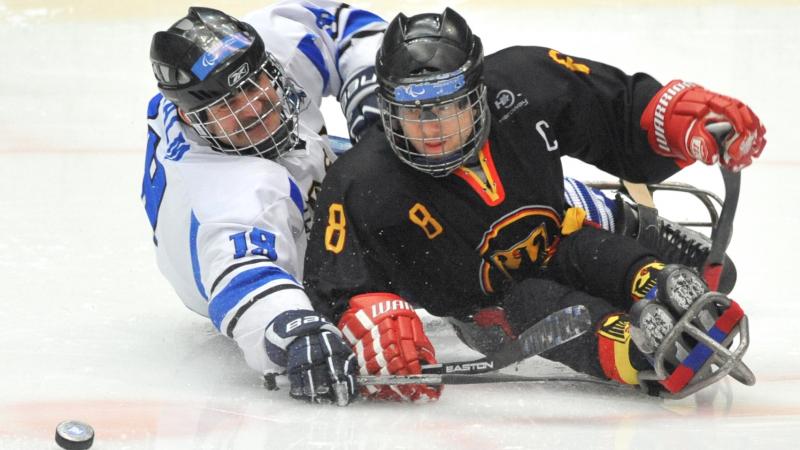 A picture of two men in sledge fighting the puck during a ice hockey match