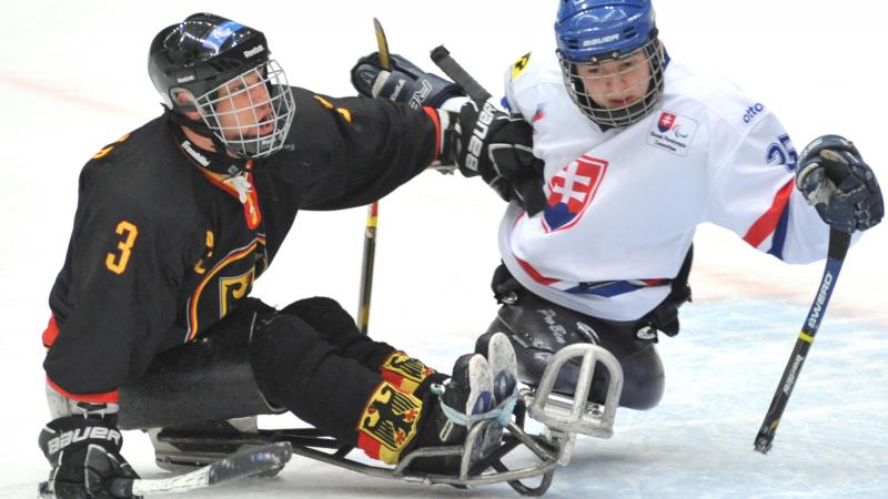 A picture of two men in sledge playing ice hockey