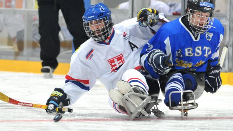 A picture of 2 men in sledge fighting the puck during a ice hockey match