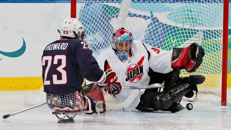 A picture of a man in sledge shooting the puck against the goalkeeper in an ice hockey match