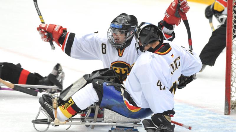A picture of 2 men in sledges celebrating a goal during a ice sledge hockey match