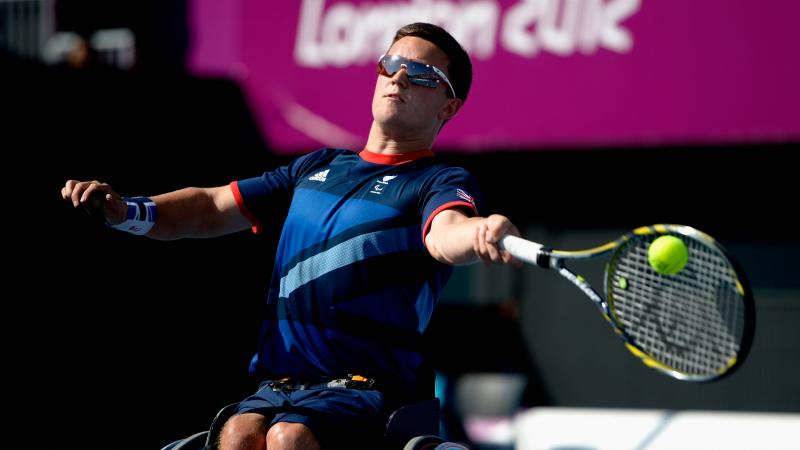 A picture of a man in a wheelchair playing a forehand during a wheelchair tennis game