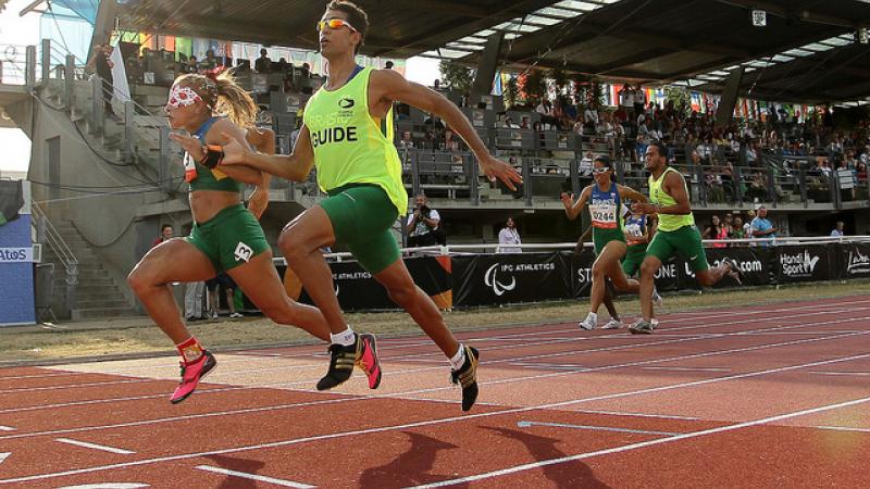 Terezinha Guilhermina and her guide run on the track of Lyon with the tribunes of the stadium in the backround