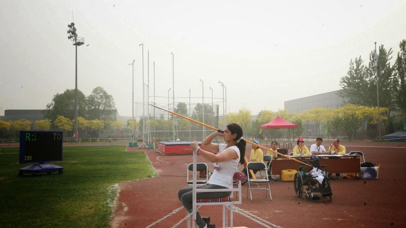 Female athlete throws the javelin from a seated position