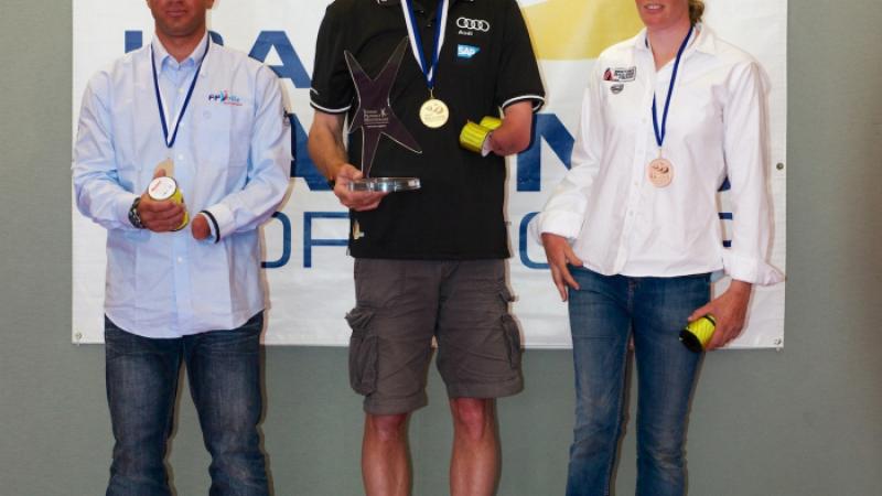 Three sailors are pictured receiving their medals on a podium. 