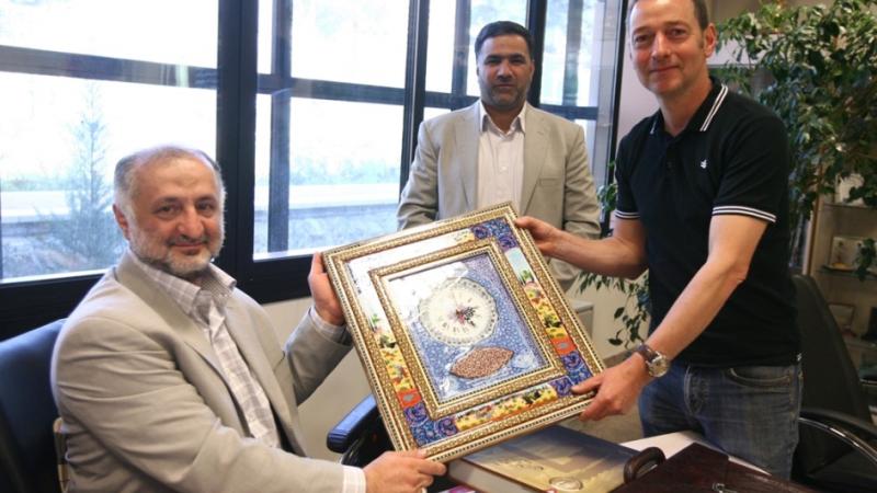 Two NPC Iran officials and reporter Ned Boulting hold up a framed award. 