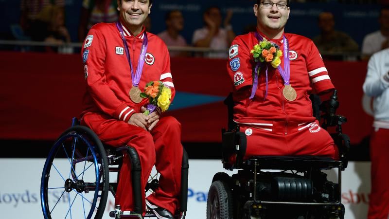 Two boccia player sit in the wheelchairs with their medals around their neck.