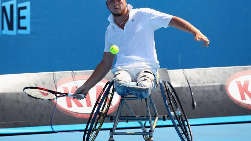 A wheelchair tennis player hits a forehand with his right hand. 