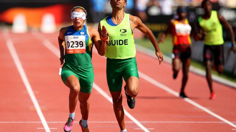 A visually impaired athlete runs with her guide on the track of a stadium.