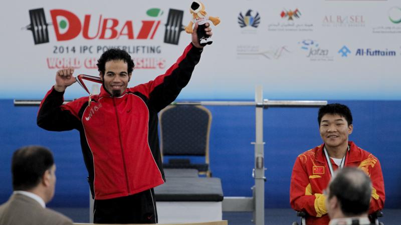 An athlete shows off his medal to a crowd, holding up a stuffed animal mascot with the other hand. 