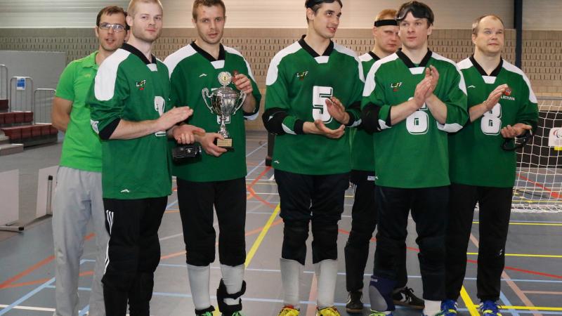 A goalball team faces the camera with their tournament trophy.