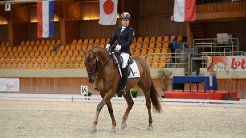 An equestrian rider rides her horse in an empty arena. 