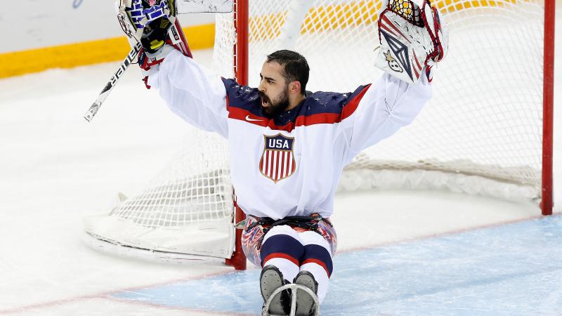 An ice sledge hockey goaltender raises his arms in celebration.