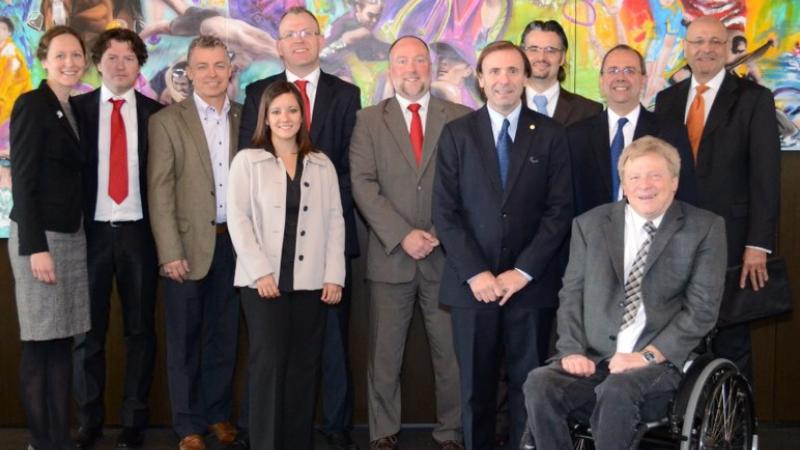 A group shot of 11 smartly dressed people lined up in front of a painted sport wall mosaic looking directly at the camera