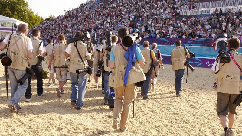 A group of photographers' backs are shown as the walk across an equestrian venue.